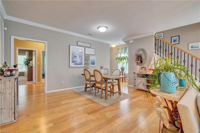 dining area featuring stairway, light wood-style flooring, ornamental molding, a textured ceiling, and baseboards