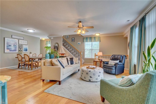 living area with visible vents, light wood-style flooring, ornamental molding, baseboards, and stairs