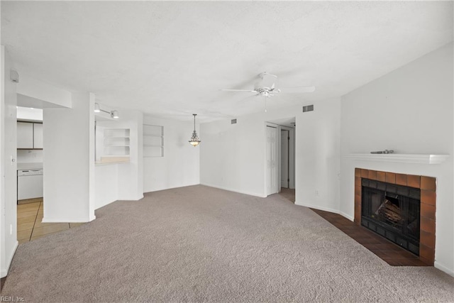 unfurnished living room with carpet floors, visible vents, a tiled fireplace, and a ceiling fan