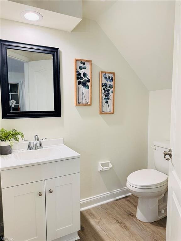 bathroom with toilet, wood finished floors, vanity, baseboards, and vaulted ceiling