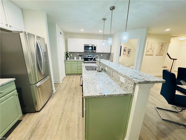 kitchen with green cabinetry, a sink, stainless steel appliances, light wood-style floors, and backsplash