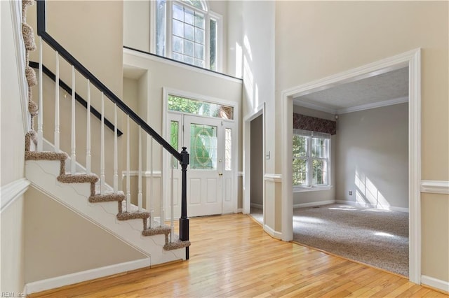 foyer featuring wood finished floors, a towering ceiling, baseboards, ornamental molding, and stairway