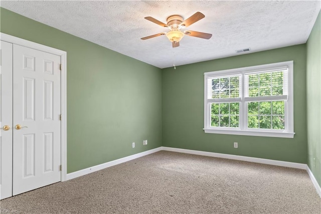 unfurnished room with a textured ceiling, carpet floors, visible vents, and baseboards