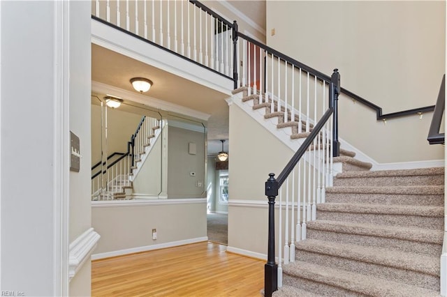 stairway featuring ornamental molding, a high ceiling, wood finished floors, and baseboards