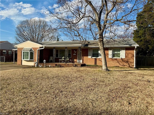 single story home with covered porch, a front yard, fence, and brick siding