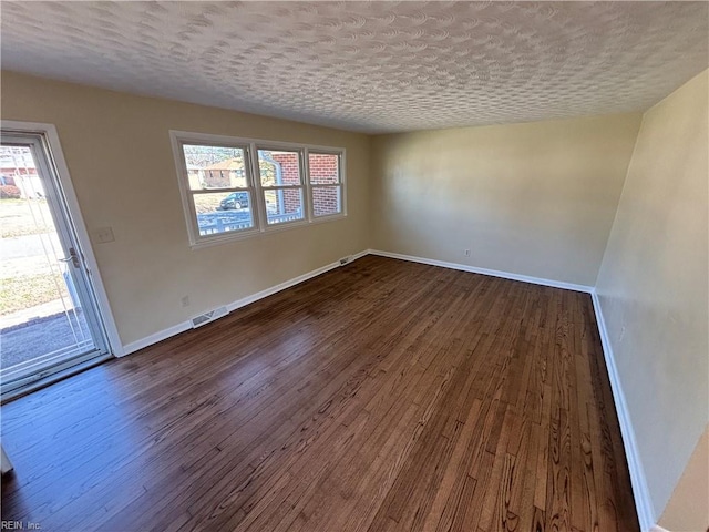 empty room with dark wood-type flooring, visible vents, and baseboards