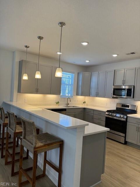 kitchen featuring gray cabinetry, a peninsula, a sink, appliances with stainless steel finishes, and a kitchen bar