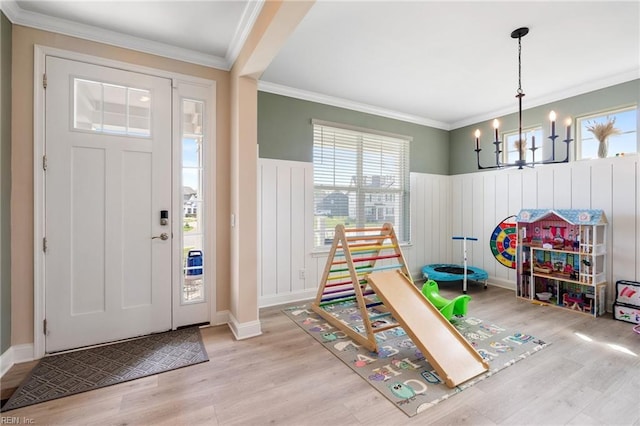 entrance foyer featuring a chandelier, ornamental molding, wainscoting, and wood finished floors