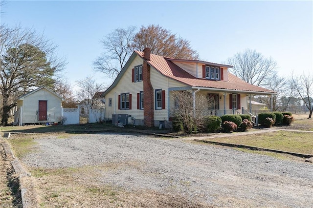 view of front facade featuring a chimney, covered porch, metal roof, fence, and driveway