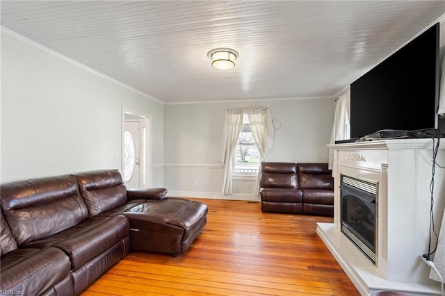 living room with a fireplace with raised hearth, ornamental molding, and light wood-style flooring