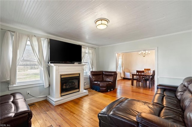 living area featuring baseboards, a glass covered fireplace, light wood-style flooring, ornamental molding, and a chandelier