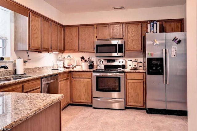 kitchen with appliances with stainless steel finishes, brown cabinetry, a sink, and light stone countertops