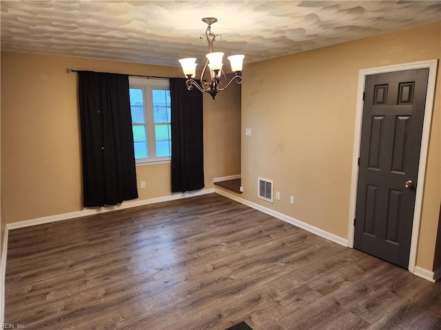 spare room featuring visible vents, a textured ceiling, wood finished floors, a chandelier, and baseboards