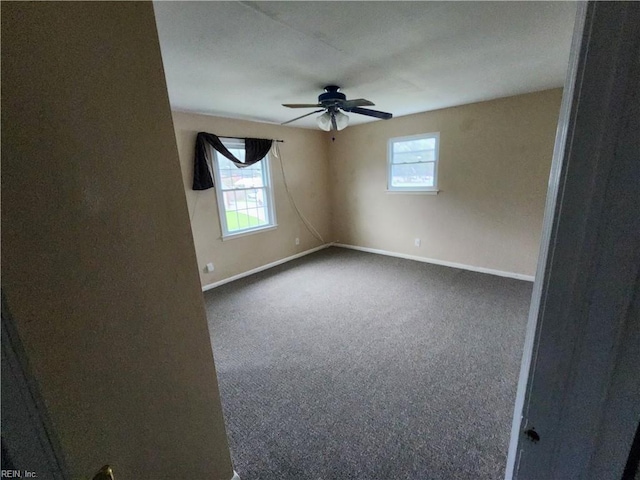 empty room featuring ceiling fan, dark colored carpet, a wealth of natural light, and baseboards