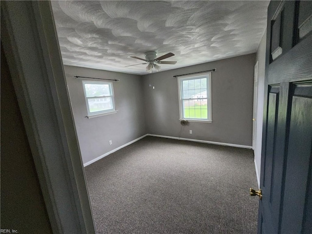 carpeted empty room with a textured ceiling, baseboards, and a ceiling fan