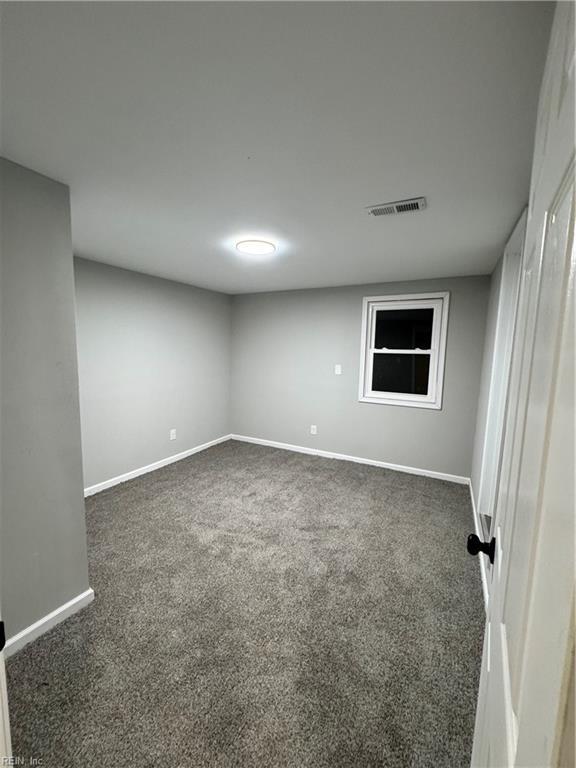 spare room featuring dark colored carpet, visible vents, and baseboards