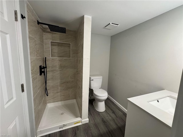 bathroom featuring baseboards, toilet, wood finished floors, a tile shower, and vanity