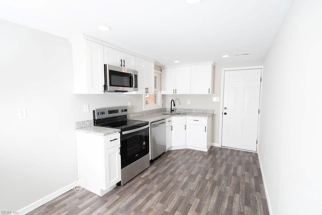 kitchen with wood finished floors, appliances with stainless steel finishes, a sink, and white cabinetry