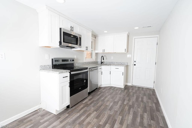 kitchen featuring stainless steel appliances, wood finished floors, a sink, white cabinetry, and light stone countertops