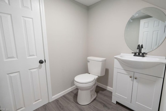 half bathroom featuring wood finished floors, vanity, toilet, and baseboards