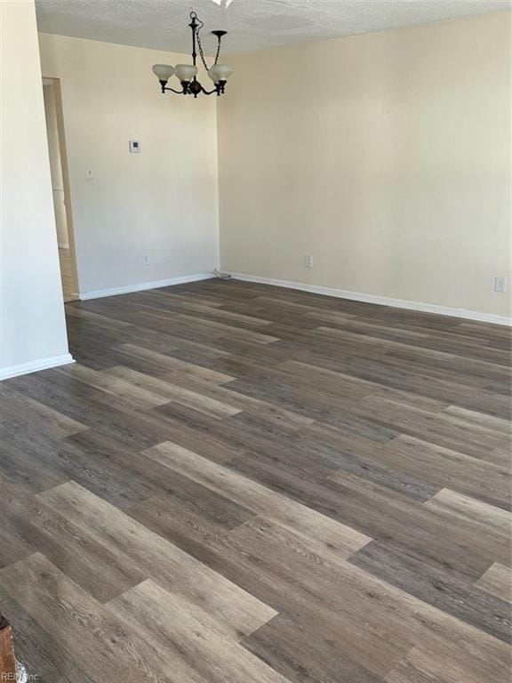 unfurnished dining area featuring baseboards, a textured ceiling, an inviting chandelier, and wood finished floors