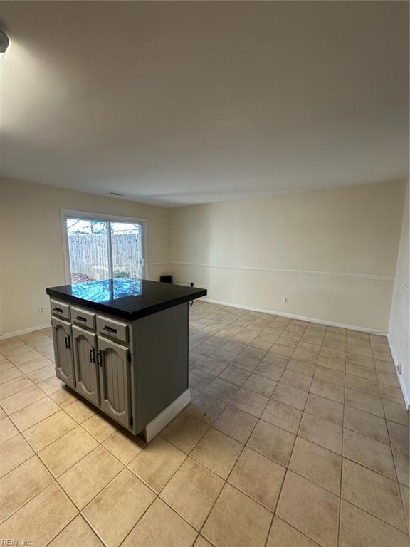 kitchen with light tile patterned floors, baseboards, dark countertops, a kitchen island, and open floor plan