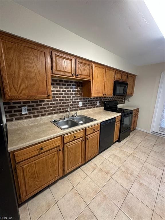 kitchen with light tile patterned floors, brown cabinetry, light countertops, black appliances, and a sink