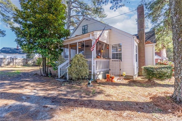 view of front of home with covered porch, a chimney, and fence