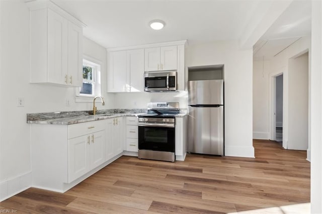 kitchen featuring appliances with stainless steel finishes, light wood-style floors, white cabinetry, a sink, and light stone countertops