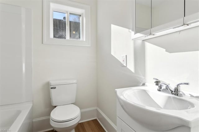 bathroom featuring a tub to relax in, toilet, vanity, wood finished floors, and baseboards