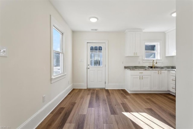 kitchen featuring baseboards, light stone counters, wood finished floors, white cabinetry, and a sink