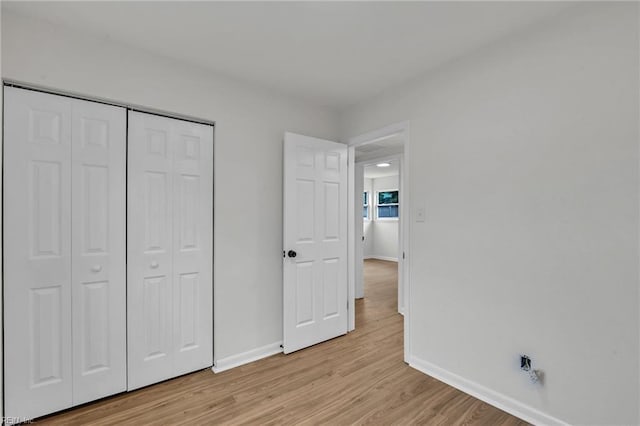 unfurnished bedroom featuring a closet, light wood-style flooring, and baseboards