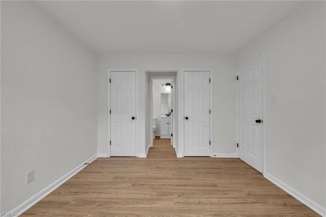 unfurnished bedroom with light wood-type flooring, baseboards, and ensuite bath