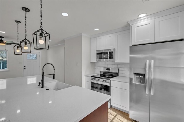 kitchen featuring tasteful backsplash, white cabinets, stainless steel appliances, light countertops, and a sink