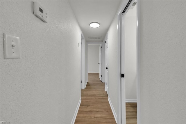 corridor featuring baseboards, visible vents, wood finished floors, and a textured wall