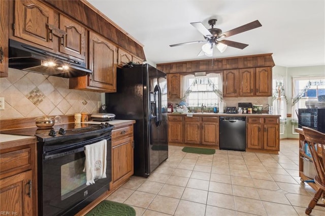 kitchen with black appliances, under cabinet range hood, a wealth of natural light, and light tile patterned flooring