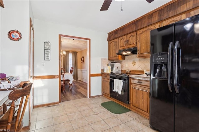 kitchen featuring light tile patterned flooring, under cabinet range hood, a wainscoted wall, light countertops, and black appliances