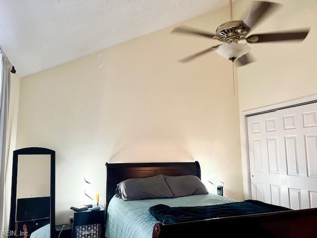 bedroom with lofted ceiling, ceiling fan, a closet, and a textured ceiling