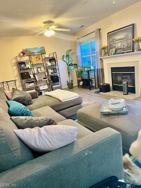 living area featuring ceiling fan, wood finished floors, a textured ceiling, and a fireplace with flush hearth