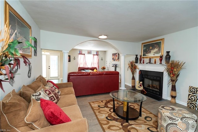 living room with arched walkways, decorative columns, a fireplace with flush hearth, wood finished floors, and baseboards