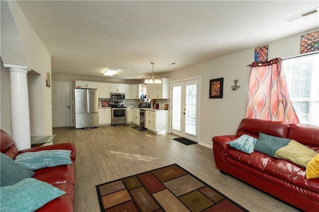 living area featuring french doors, light wood-type flooring, visible vents, and ornate columns