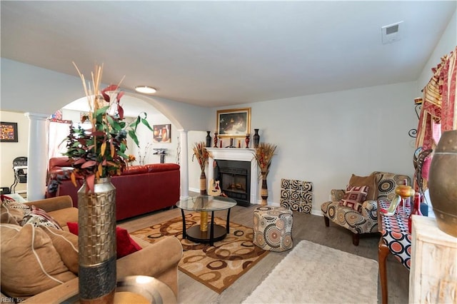 living room with decorative columns, arched walkways, visible vents, wood finished floors, and a fireplace