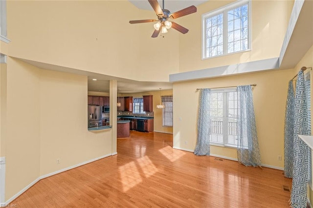 unfurnished living room featuring a towering ceiling, light wood-style flooring, baseboards, and a ceiling fan