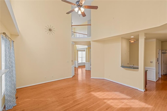 unfurnished living room with a towering ceiling, a ceiling fan, baseboards, and wood finished floors