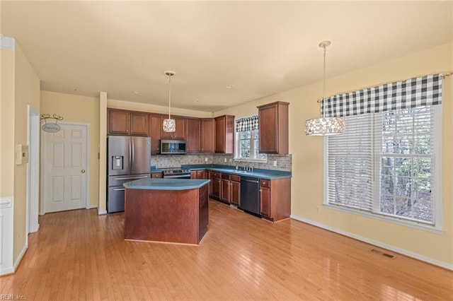 kitchen featuring tasteful backsplash, light wood-style flooring, appliances with stainless steel finishes, a center island, and pendant lighting