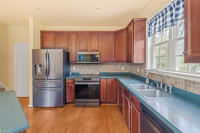 kitchen featuring appliances with stainless steel finishes, a sink, light wood-style flooring, and decorative backsplash