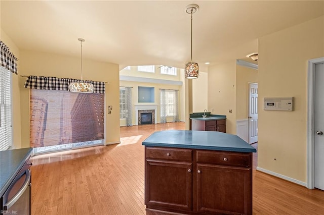 kitchen featuring light wood-type flooring, a glass covered fireplace, a sink, and dark countertops