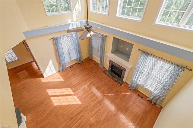 living room with visible vents, a ceiling fan, a towering ceiling, a premium fireplace, and wood finished floors