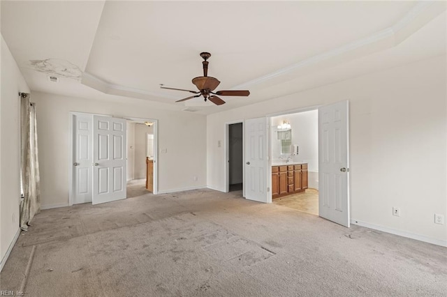 unfurnished bedroom with ensuite bathroom, ceiling fan, light colored carpet, baseboards, and a raised ceiling