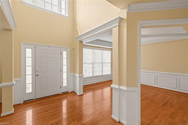 entrance foyer with a wainscoted wall, ornamental molding, wood-type flooring, and ornate columns